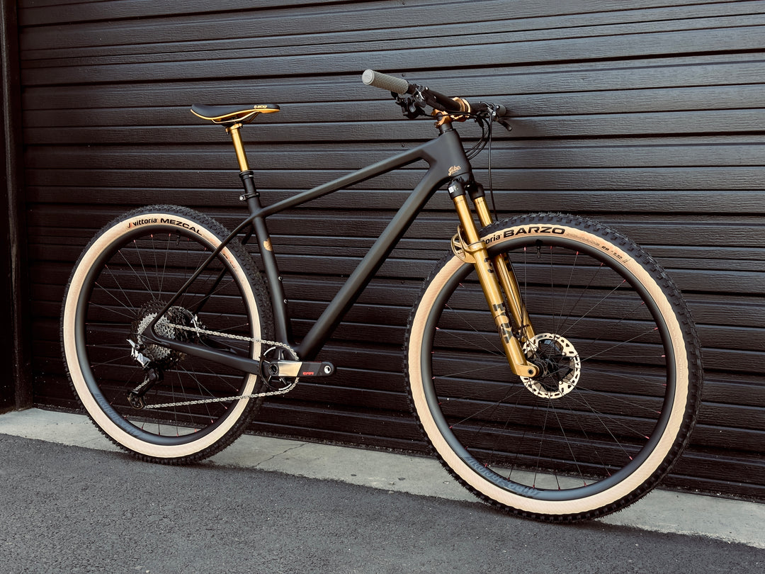 Jibe XCHT lightweight carbon fiber hardtail race bike with Shimano XTR brakes, rear derailleur, cassette, raceface era cranks, fox podium 32 stepcast fork in kashima color. Jibe Factory wheels with sapim spokes and matching SDG saddle and lizard skin clamp on grips