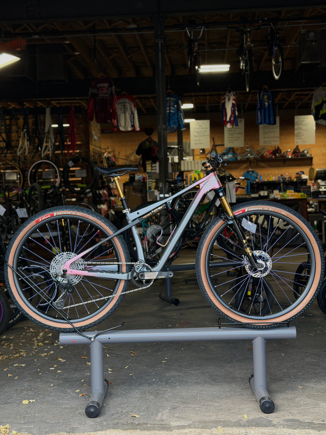 Bicycle on a stand in a bike shop with various bikes and equipment in the background.