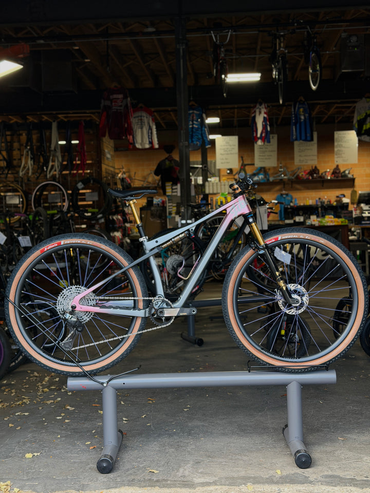 Bicycle on a stand in a bike shop with various bikes and equipment in the background.