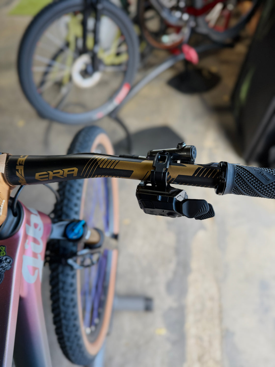 Close-up of a bicycle handlebar with a visible brand logo, blurred background of other bikes.