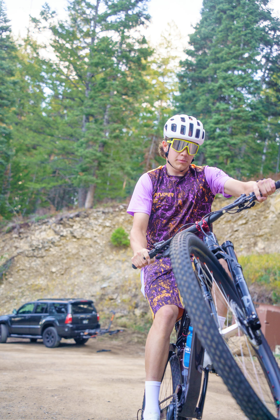 Person wheelieing a mountain bike in a forested area with a truck in the background
