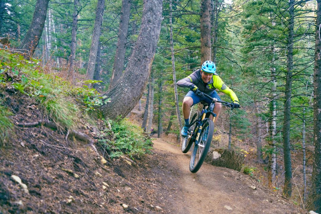 Man jumping a mountain bike, in the Utah forest with a Jibe green jacket. 